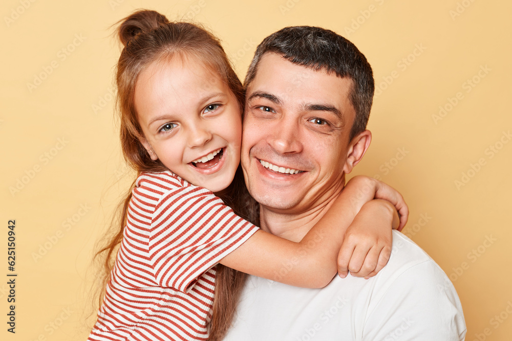 Joyful family father and daughter wearing casual t-shirts standing hugging each other looking at camera with happy faces isolated over beige background Joyful family father and daughter wearing casual t-shirts standing hugging each other looking at camera with happy faces isolated over beige background