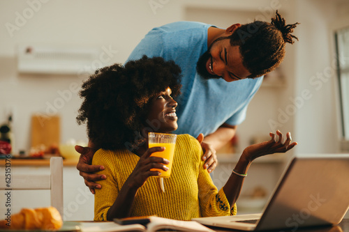 A happy african american female freelancer is taking a break from a remote job from home while her husband is embracing and supporting her.