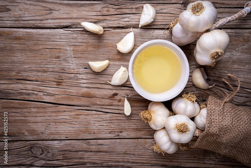 Ripe and raw garlic and garlic oil in glass of bottle on wooden table with burlap sack, alternative medicine, organic cleaner.