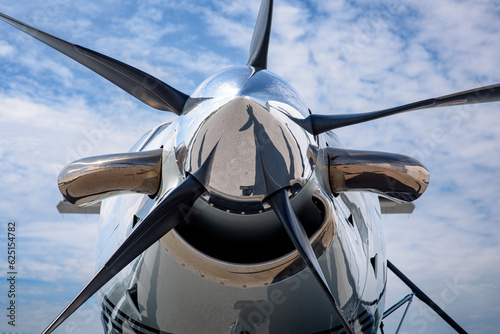 Detail of the spinner, blades, exhaust and intake of a turboprop aircraft. Chrome nose cone and propeller in the front with a blue skies and high cirrus clouds in the background.