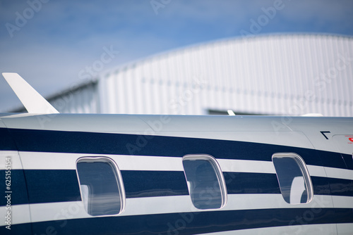 Detail of the fuselage of a Pilatus PC-12 with a hangar in the background. Shallow depth of field.