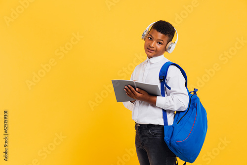 Happy african schoolboy wearing headphones and backpack holding books and notebooks. Back to school concept.
