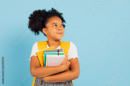 Happy African American schoolgirl holding books on blue background, back to school concept. photo