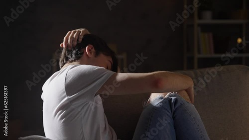 Sad teenager boy sitting on sofa. Depression, anxiety and loneliness concept.