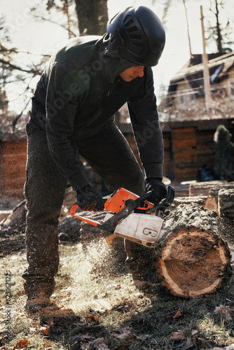Woodcutter saws tree trunk with chainsaw. Sawdust flies from chainsaw.