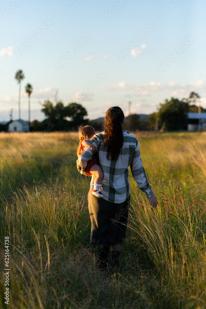 Young mum with toddler in rural country setting going for walk in farm paddock on autumn afternoon Young mum with toddler in rural country setting going for walk in farm paddock on autumn afternoon