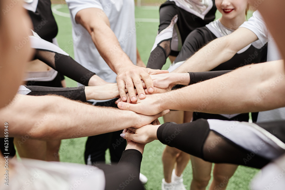 Close-up of cheerleaders and their coach holding hands together to support each other before competition