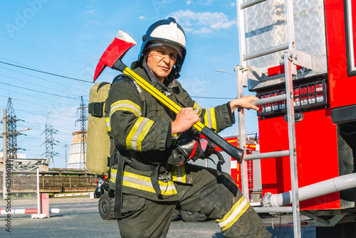 A firefighter wearing a helmet and protective clothing with a breathing apparatus holds an axe on his shoulder.A firefighter is holding onto the ladder step of a fire truck.A lifeguard with a fire axe