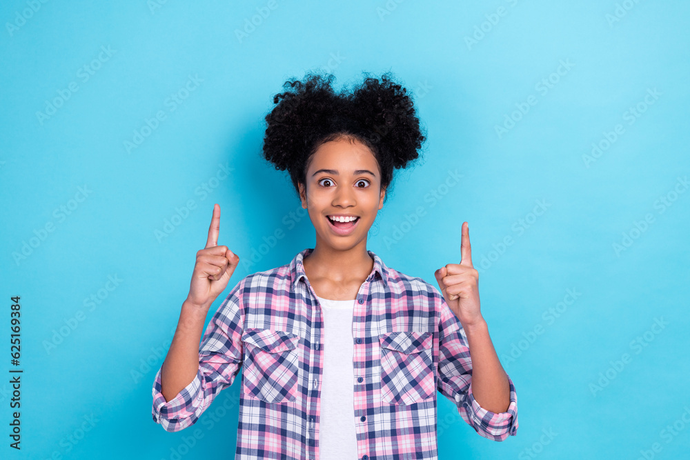Portrait of impressed person with afro hairstyle wear plaid shirt indicating at offer empty space isolated on blue color background Portrait of impressed person with afro hairstyle wear plaid shirt indicating at offer empty space isolated on blue color background