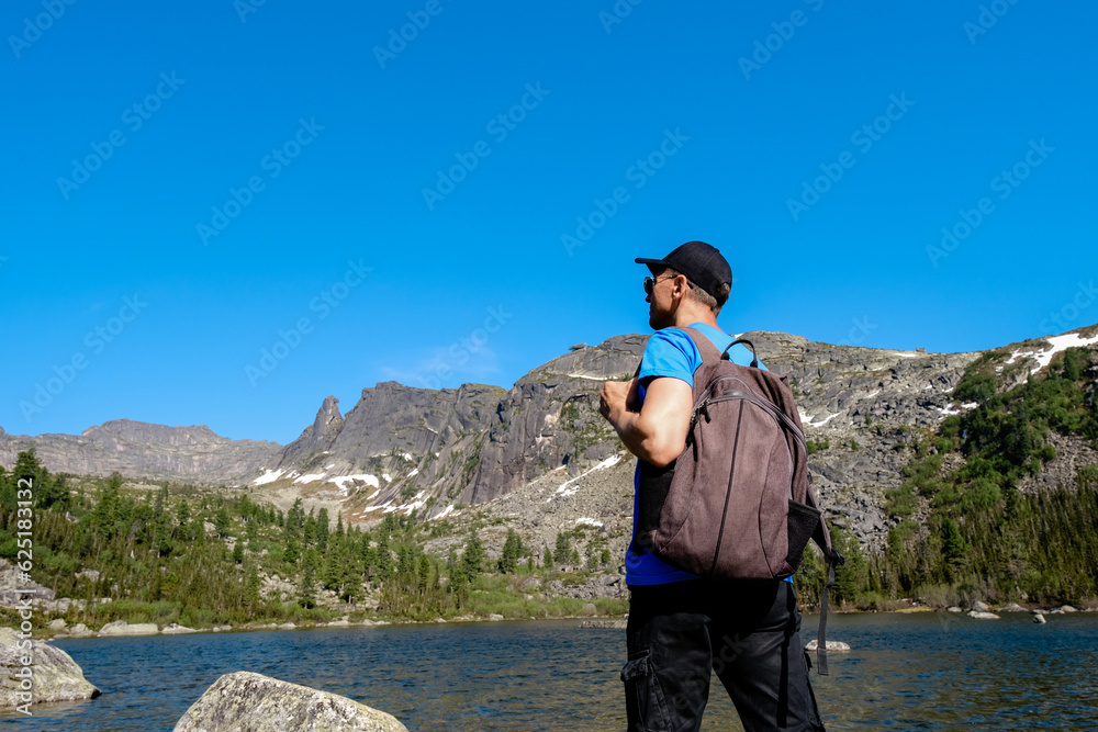 Backpacker standing on nature and admiring picturesque scenery of mountains and lake under cloudy sky in daylight