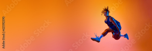 Athletic young man, basketball player in motion, jumping with ball against orange background in neon lights. Concept of professional sport, competition, hobby, competition. Banner. Copy space for ad