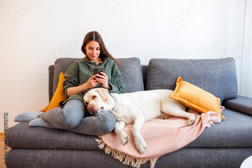 Woman having phone conversation and cuddling her dog at home