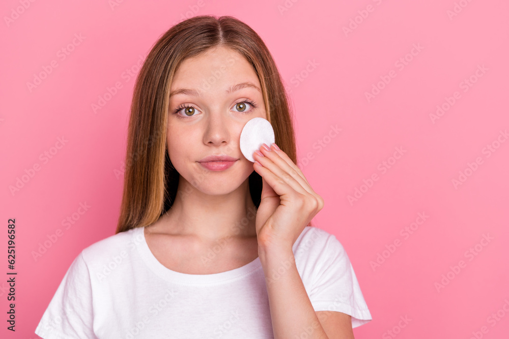 Portrait of cute teenager girl hand hold cotton disk touch cheek empty space wear white t-shirt isolated on pink color background Portrait of cute teenager girl hand hold cotton disk touch cheek empty space wear white t-shirt isolated on pink color background