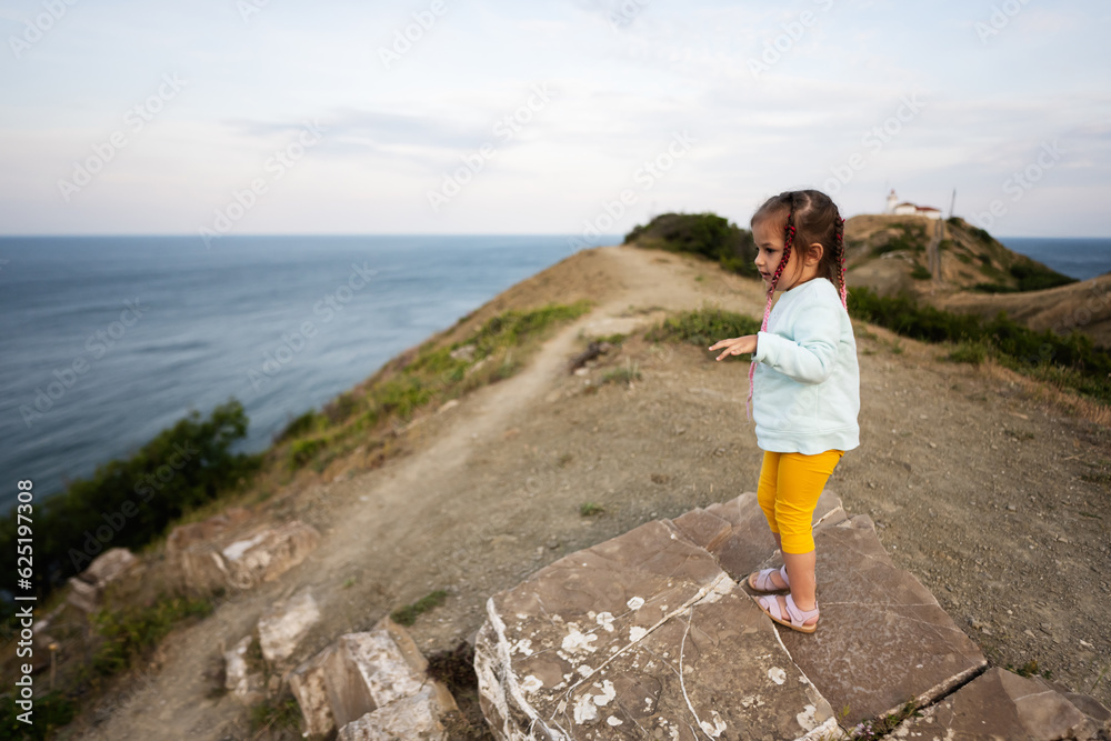 Cute little girl standing on top of a cliff and looking at the sea. Cape Emine, Black sea coast, Bulgaria.