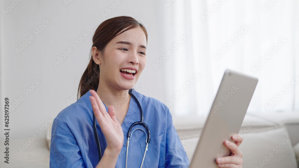 Smiling young Asian female doctor or nurse waving hands while using tablet video call online with patient. Female doctor geeting patient while consulting online through tablet Smiling young Asian female doctor or nurse waving hands while using tablet video call online with patient. Female doctor geeting patient while consulting online through tablet