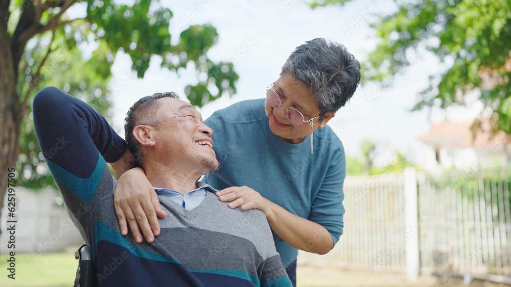 Happy asian elderly married couple relaxing in park together. Cheerful asian adult male patient sitting on wheelchair and senior wife enjoying leisure. Relationship concept Happy asian elderly married couple relaxing in park together. Cheerful asian adult male patient sitting on wheelchair and senior wife enjoying leisure. Relationship concept