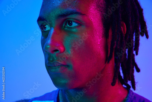 Portrait of young man, professional athlete, basketball player posing against gradient blue background in neon lights. Concept of professional sport, competition, hobby, game, competition, ad