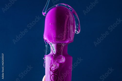 Intimate lubricant pours on a purple vibrator on a blue background. Copy space. 
