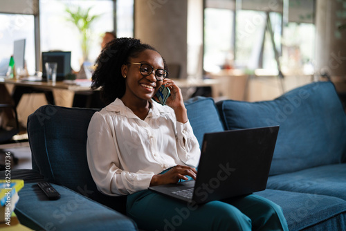 Black businesswoman working on laptop. Portrait of beautiful businesswoman talking to the phone in the office.