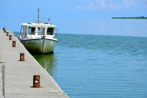 A close up on a small passenger or fishing boat parked next to a concrete part of a marina or jetty, next to some small channel covered with reeds, trees and other flors spotted in Poland in summer photo