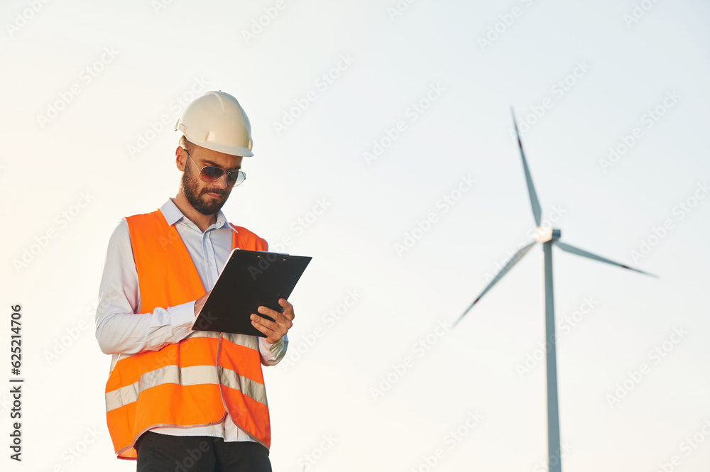 With notepad. Service engineer is on the field with windmills With notepad. Service engineer is on the field with windmills