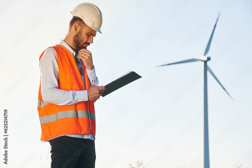 With notepad. Service engineer is on the field with windmills With notepad. Service engineer is on the field with windmills