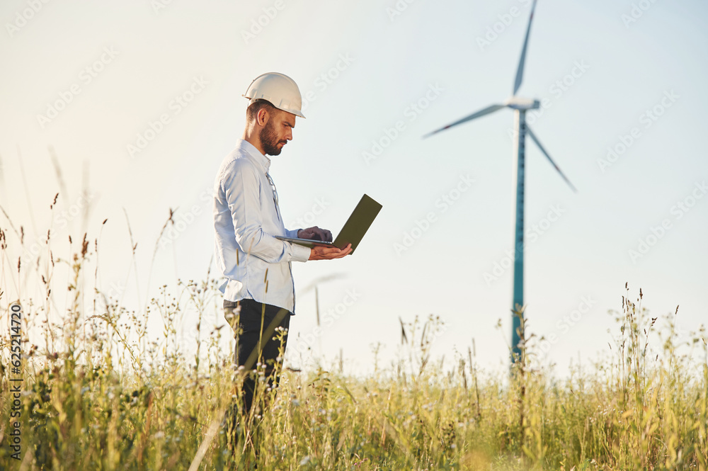 Working by using laptop. Service engineer is on the field with windmills Working by using laptop. Service engineer is on the field with windmills