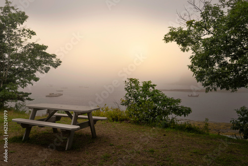 Foggy morning seascape with empty bench and table on the green hill at Boothbay Harbor in Lincoln County  Maine