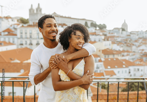Smiling young african american guy hugging lady in dress, look at copy space in city #625216329