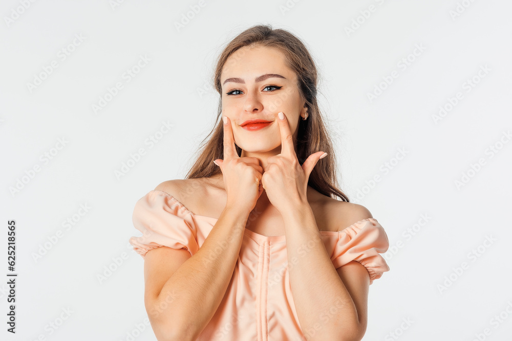 Naklejka premium Put on your smile. Pretty young woman holding fingers on her mouth and making fake smile, posing against white studio background