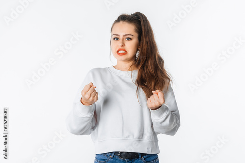 Pissed-off girl gesticulating with her hands, stands over white background. Distressed and irritated female in white sweatshirt squeeze hands in fists losing patience, boiling from annoyance photo