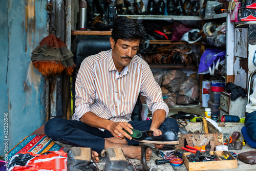 Indian man repairs shoes on the street also called shoemaker, cobbler or mochi photo