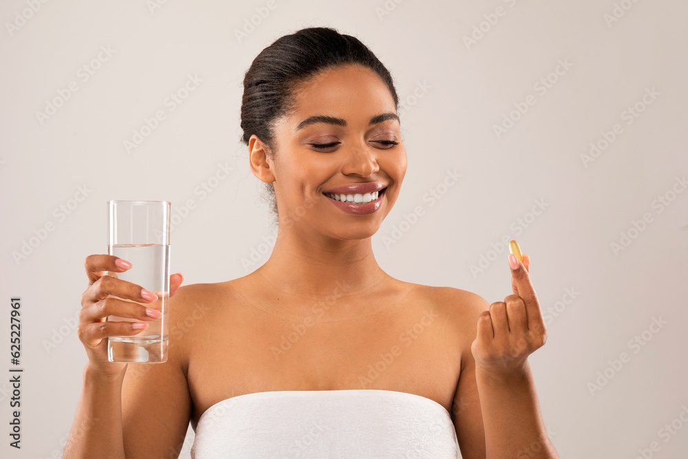 Beautiful young black woman taking beauty pill, grey background Beautiful young black woman taking beauty pill, grey background