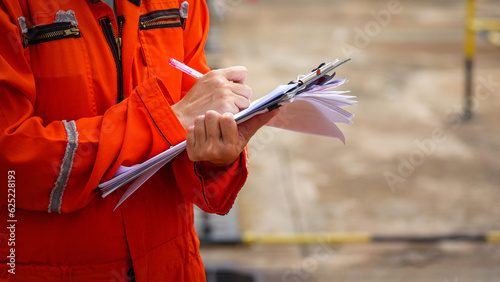 Fotografia Action of a safety officer in full PPE coverall is writing note on paper document during perform safety audit at construction worksite