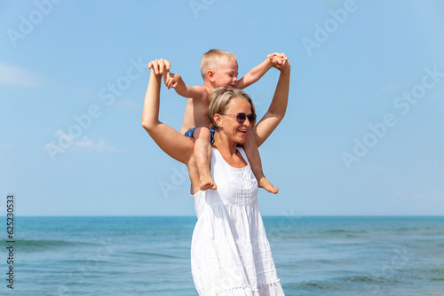 A young woman with a little boy are walking along the seashore on a sunny day. Happy mom and son on vacation hug and laugh. Love and tenderness. Travel, tourism and recreation.