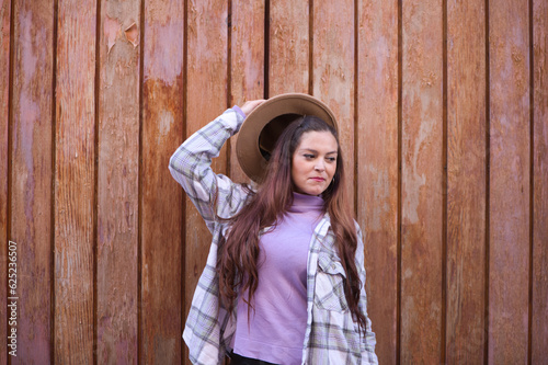 Young and beautiful Spanish woman from Seville with brown hair, hat and checkered shirt standing on a wooden door in different poses and expressions.