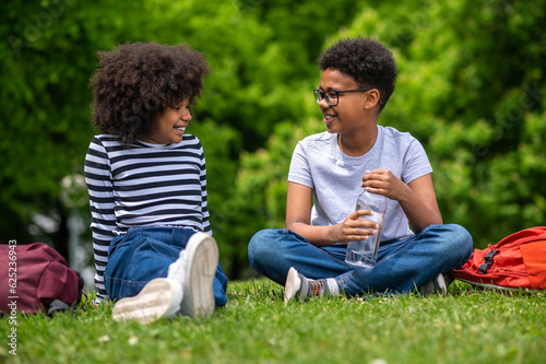 Two african american kids sitting on the grass in the park