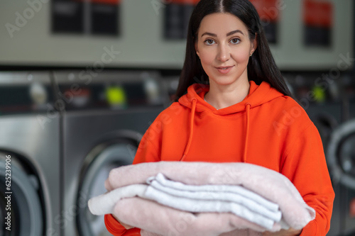 Laundry service. Brunette adult woman holding washed towels in public laundry.