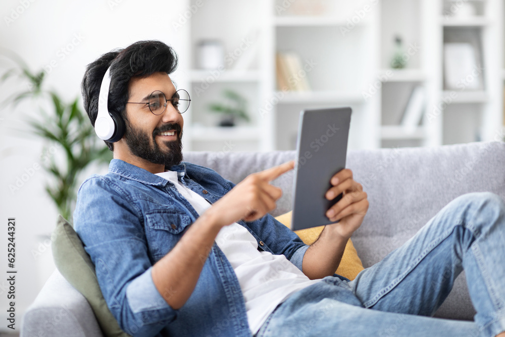 Smiling Indian Man Wearing Wireless Headphones Resting With Digital Tablet At Home Smiling Indian Man Wearing Wireless Headphones Resting With Digital Tablet At Home