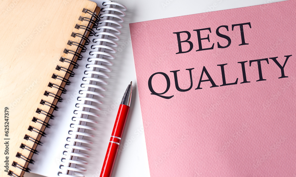 BEST QUALITY word on the pink paper with office tools on white background BEST QUALITY word on the pink paper with office tools on white background