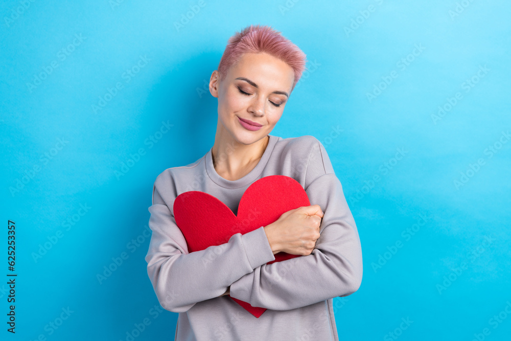 Photo of peaceful lovely girl closed eyes hands hold hug red paper heart symbol card isolated on blue color background Photo of peaceful lovely girl closed eyes hands hold hug red paper heart symbol card isolated on blue color background