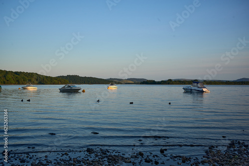 Fototapeta Naklejka Na Ścianę i Meble -  Loch Lomond - Tranquil sunset scene with boats peacefully sailing on serene water, embraced by fading light and complemented by a playful kite.