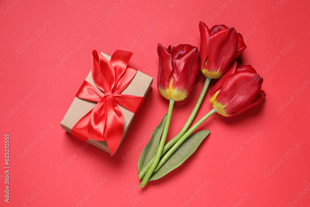 Beautiful gift box and tulips on red background, flat lay