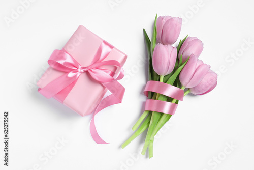 Beautiful gift box with pink bow and tulips on white background, flat lay