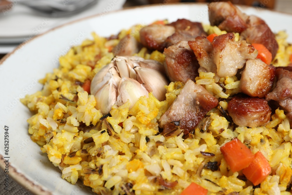 Delicious pilaf with meat, carrot and garlic on plate, closeup Delicious pilaf with meat, carrot and garlic on plate, closeup