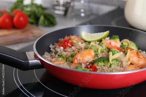 Tasty rice with shrimps and vegetables in frying pan on induction stove, closeup