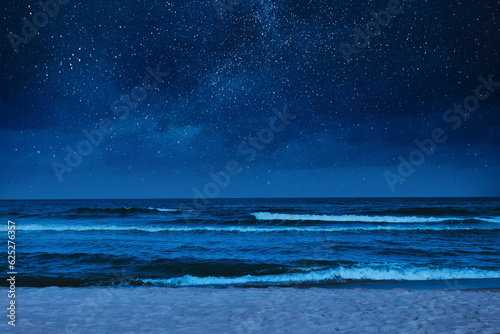 Sea waves rolling onto sandy beach under starry sky at night