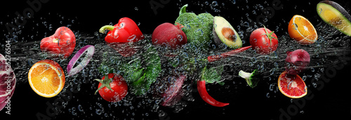 Many fruits and vegetables falling into water against black background
