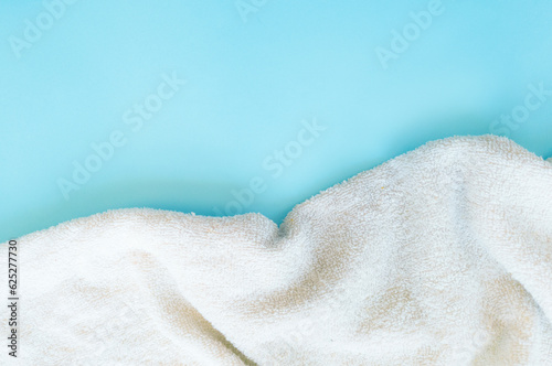 A white towel laid scattered on a blue background, with free space for text. Suitable for a pleasant vacation, for a happy holiday. In the atmosphere of a summer sale