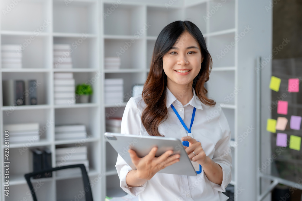 Attractive Asian businesswoman standing happily using tablet at work and smiling happily. Attractive Asian businesswoman standing happily using tablet at work and smiling happily.